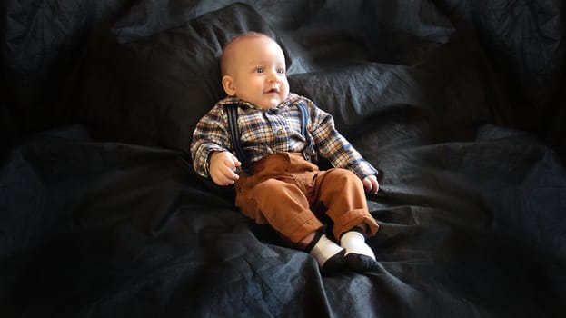 A kid in mustard pants and a plaid shirt lies on a black background. High quality photo