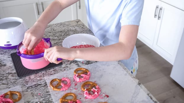 With focused attention, this budding culinary artist dips pretzels into a pot of melted chocolate, creating sweet delights in the warmth of a well-lit home kitchen.