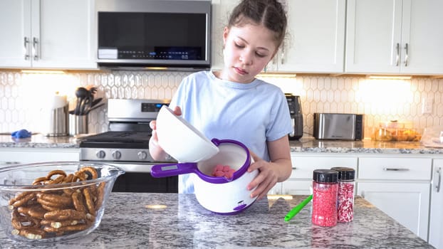 With focused attention, this budding culinary artist dips pretzels into a pot of melted chocolate, creating sweet delights in the warmth of a well-lit home kitchen.