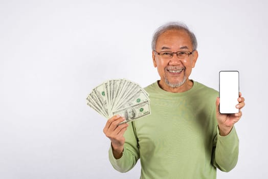 Portrait Asian smiling old man is holding a bunch of money fan and showing screen of mobile phone studio shot isolated on white background. happy elderly positive excited hold dollar banknotes fan