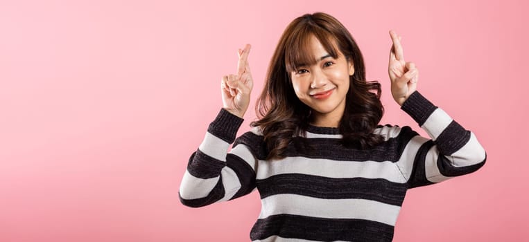 Asian happy portrait beautiful cute woman smile have superstition her holding fingers crossed for good luck or lie gesture studio shot isolated on pink background, young female fraud hope for better