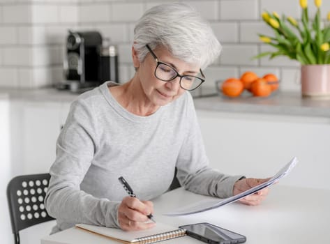 Mature Woman Examines Documents And Makes Notes At Home