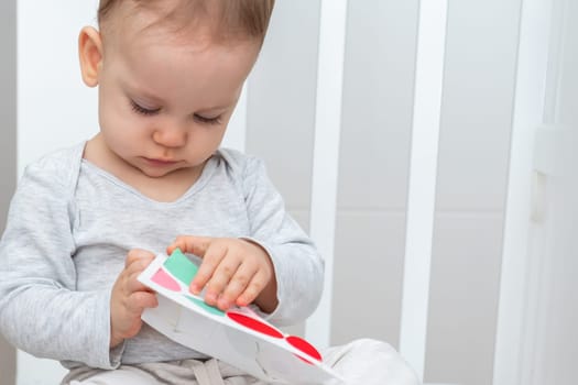 Baby girl playing with montessori busy book sitting in a crib