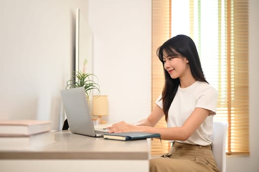 Charming young woman in casual clothing working online on laptop at home.