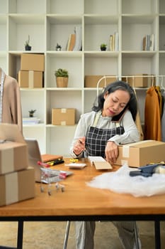 Senior female small business owner having phone conversation and calculating expense at desk.