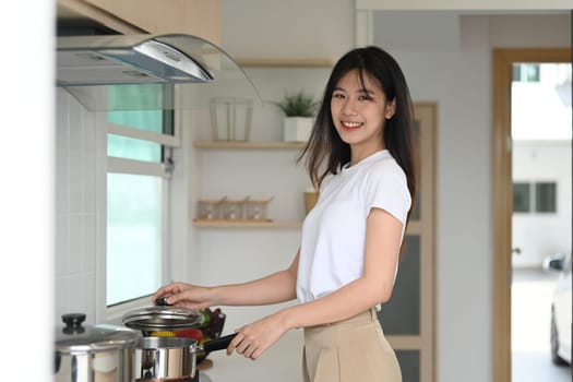 Portrait of beautiful young asian woman making a hearty soup in the kitchen and looking at camera.