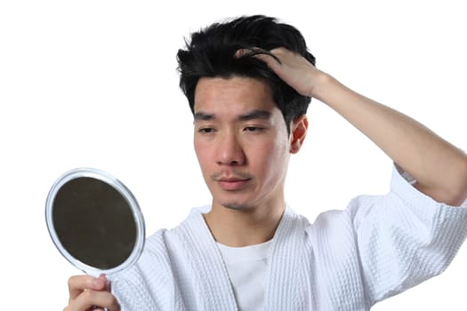 Young Asian man after facial laser treatment looking at the mirror isolated on white background.