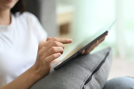 Close up young woman in casual clothes surfing internet on digital tablet at home.