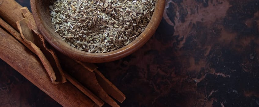 Brown wooden background.. Horizontal picture. Still life. Wooden bowl with anise seeds and cinnamon sticks.