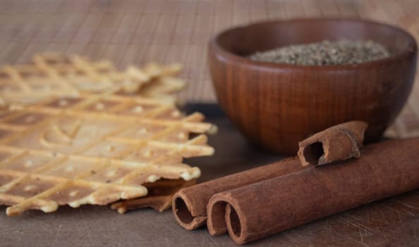 Delightful crunchy cinnamon biscuit. Still life. Wooden bowl with anise seeds and cinnamon sticks. Brown wooden background.