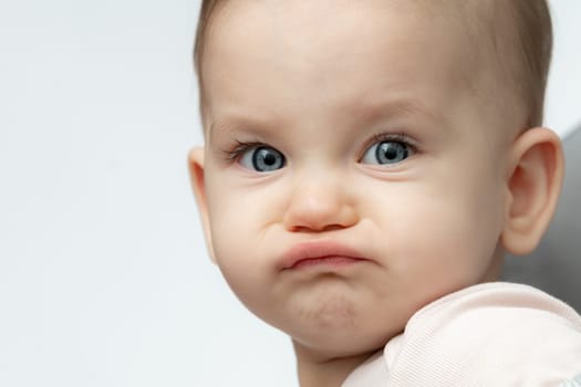 Baby makes a funny angry and sad face sitting in a chair