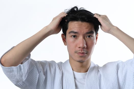 Worried man examining his head on white background. Hair loss issue and cosmetics products for men concept.