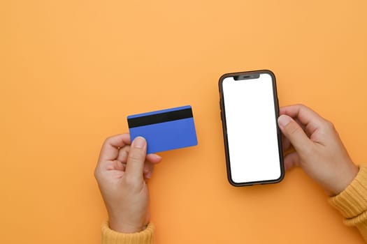 Woman hand holding mobile phone with blank screen and credit card on yellow background.