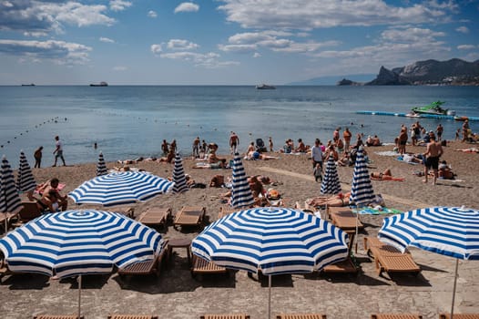 SUDAK, CRIMEA - SEPTEMBER 6, 2021: People sunbathe on beach on Black Sea coast on beach in resort town of Sudak in Crimea