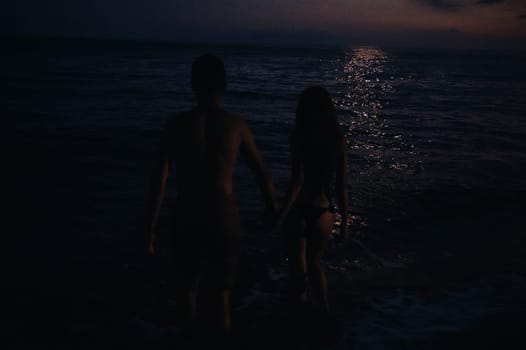 naked couple in love romantically go swimming at night in sea by beach in summer under moonlight. Atmospheric lifestyle photography with soft focus and film grain