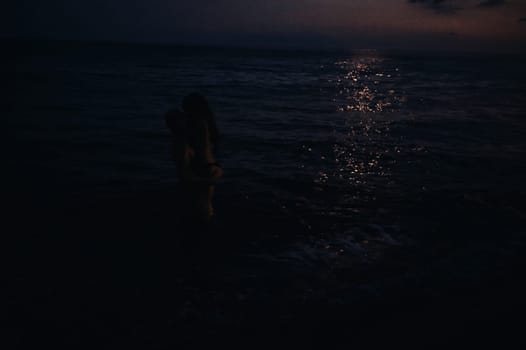 girl and boyfriend love each other, hug and kiss standing in water in sea by beach on a summer night. Atmospheric lifestyle photography with soft focus and film grain