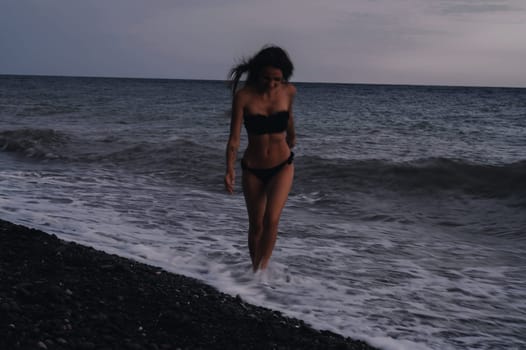 happy young girl in a swimsuit runs on sea waves on beach on a summer evening. Photo with a blur from a long exposure to give an authentic atmosphere