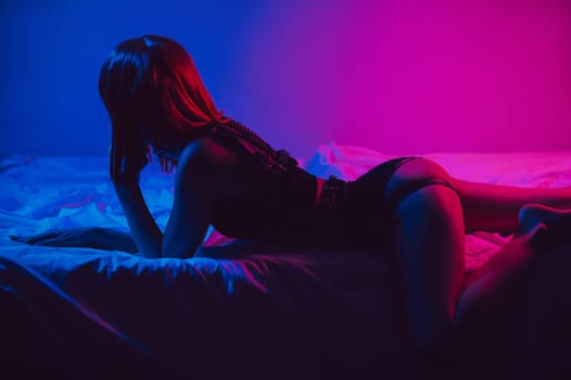 woman with sexy booty and a slender body in erotic underwear lies beautifully on bed in bedroom with neon colored light