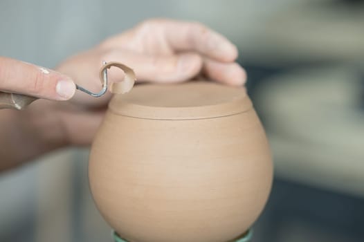 A potter works with a tool on a potter's wheel. Close-up of a man's hands