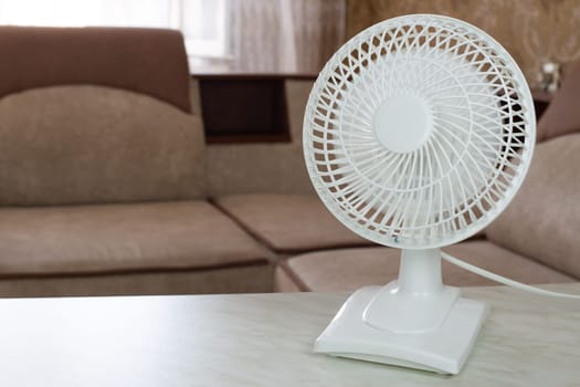 Tabletop white fan with fast rotating blades for cool air flow in home room, electronic fan for cooling on hot sunny day