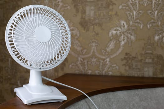Compact electric fan on sofa shelf with blades included to cool room on hot day, raise the temperature with fan for home