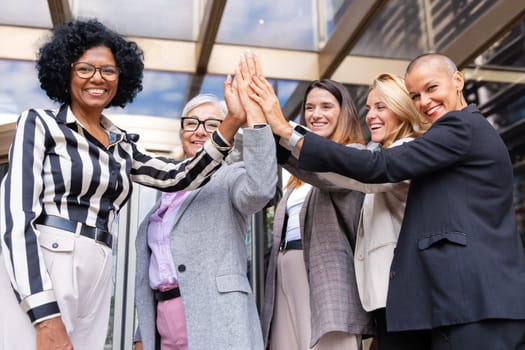 Five happy multiethnic women stacking hands in the city looking at camera