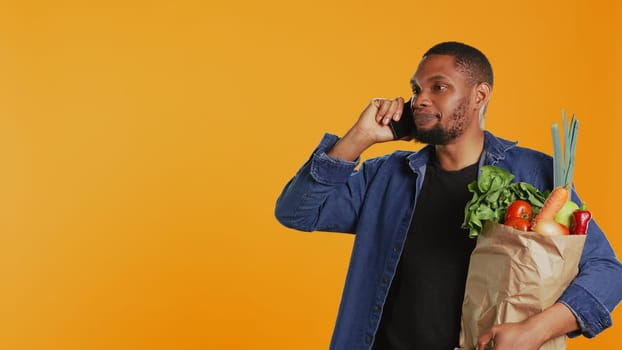 African american man on grocery shopping spree chatting on phone call, discussing with people about a new zero waste eco store in the city. Young adult recommends fresh bio produce. Camera B.