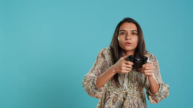 Upset woman showing thumbs down sign gesturing holding controller after being defeated in videogames. Displeased indian person doing rejection hand gesture after losing, studio background, camera A