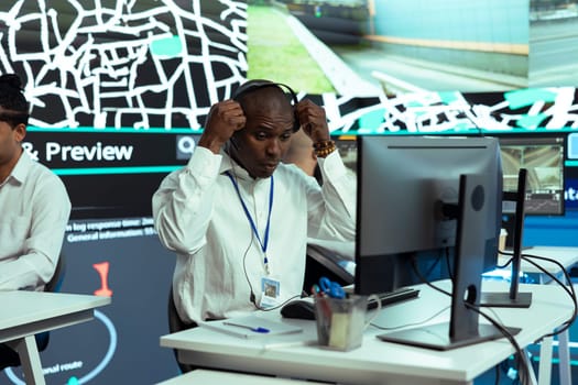 African american employee monitoring express delivery service activity through urban traffic, following couriers via gps coordinates on satellite map. Dispatch operator helps with cargo shipment.