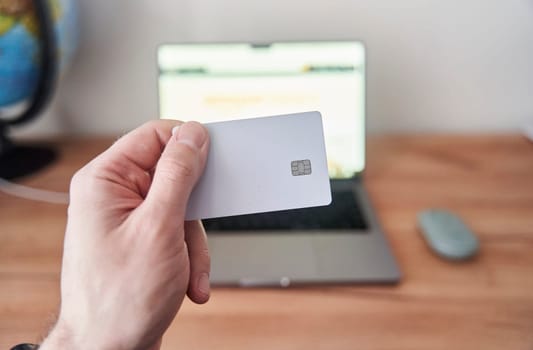 A person is holding a credit card in front of a personal computer with a laptop screen. They are using the touchpad to make a gesture