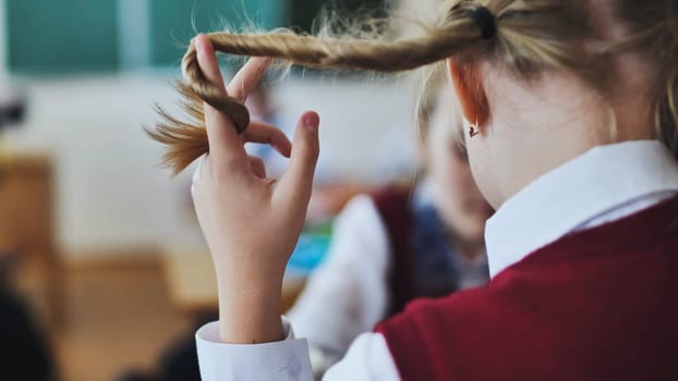 A girl touches a braid of her hair during class