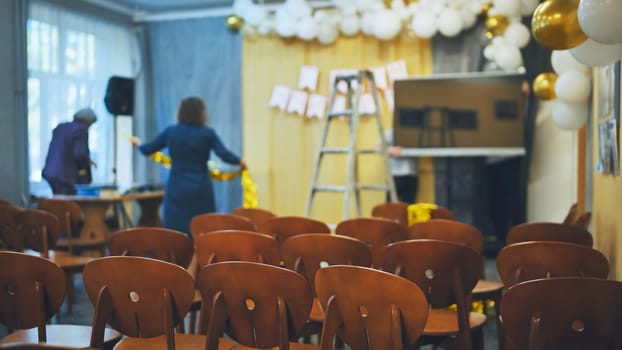 Teachers prepare the hall for a school event. Focus focus on the chairs.