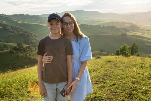 Portrait of happy mother and son tourists in a beauty mountain valley at sunset