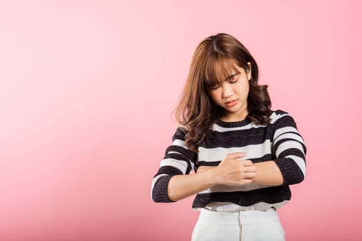 Asian beautiful woman itching her scratching her itchy arm on pink background with copy space, Medical and Healthcare concept, female skin problems scratch the itch with her arm