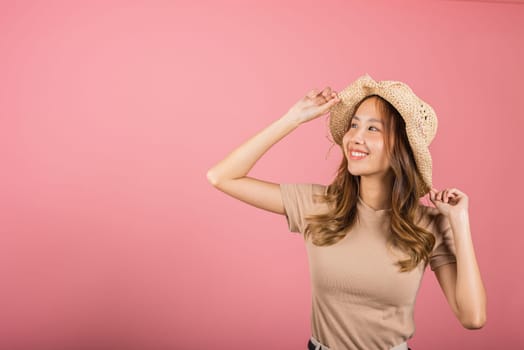 Portrait of positive Asian young woman wearing straw hat is smiling and looking up studio shot isolated on pink background, female people excited summer life enjoy in holiday lifestyle concept