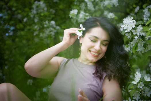 Joyous brunette woman near Blossoms of apple tree in a Spring Garden outdoors. The Concept of face and body care. The scent of perfume and tenderness