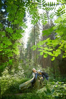 Adult mature woman 40-60 in a green long fairy dress in forest. Photo shoot in style of dryad and queen of nature. Fairy in beautiful green summer forest. Concept of caring for nature