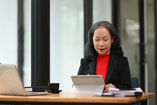 Portrait of smiling mature businesswoman using digital tablet at her office desk.