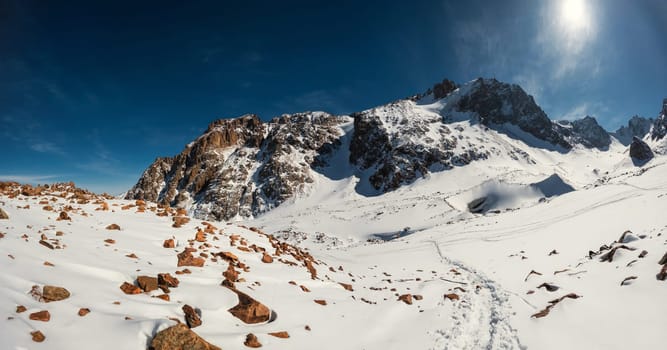 Discover the breathtaking beauty of Central Asia with a panoramic view of the Bogdanovich Glacier in Kazakhstan's Almaty Mountains. This scenic shot captures the winter wonderland on a sunny day.