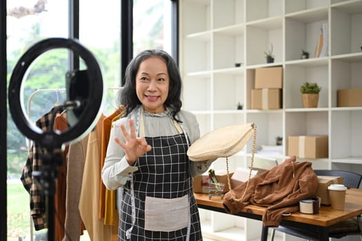 Middle age asian woman presentation bag fashion in front of the camera while live streaming at her shop.