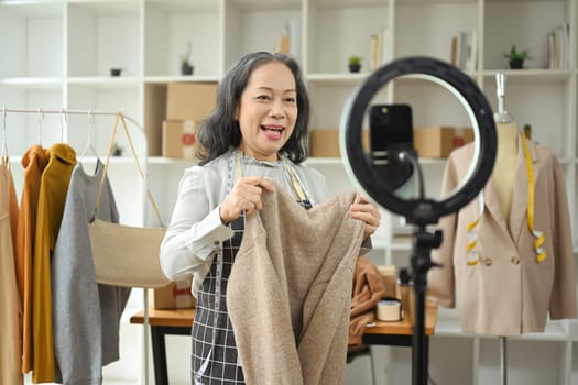 Cheerful small business owner live streaming and showing clothing to customer at her shop.