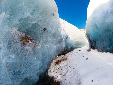 Amazing winter landscape on the way to a mountain glacier, a path surrounded by a blue transparent ice corridor interspersed with mountain stones.