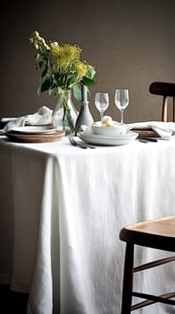 A table with a white tablecloth and a vase of flowers in the center. The table is set with plates, cups, and utensils. Scene is elegant and inviting