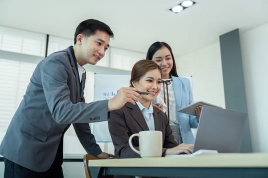 Three business colleagues in formal attire working together on a laptop during an office meeting, showcasing teamwork and corporate collaboration