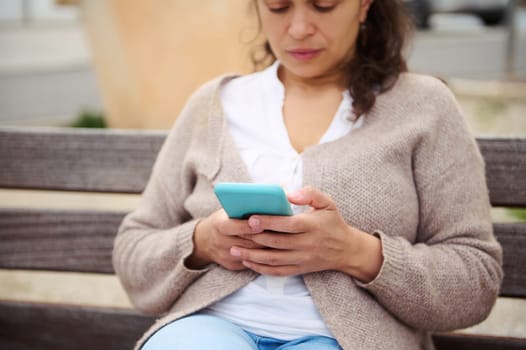 Portrait of a woman using mobile phone outdoors, sitting on a city bench