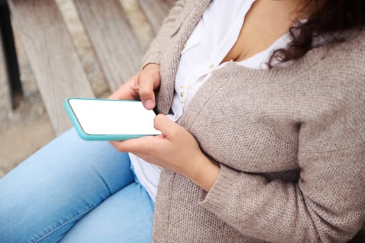 Portrait of a woman using mobile phone outdoors, sitting on a city bench. Mockup white screen