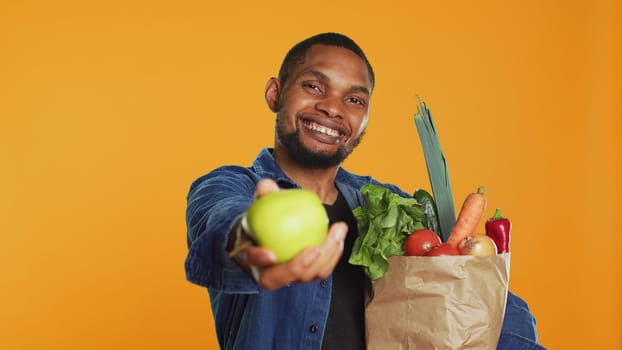 African american man presenting a freshly harvested green apple, showing the organic bio fruits in front of the camera. Happy person advocating for healthy eating and vegan nutrition. Camera A.