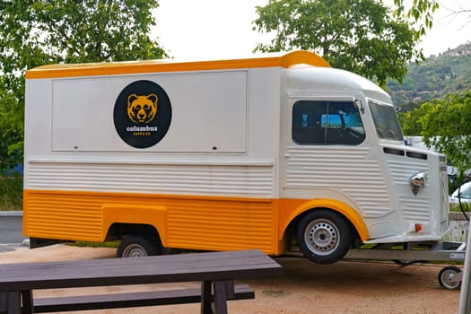 La Turbie, France - June 12, 2023: A white and yellow food truck with a bear logo is parked in front of a picnic table.
