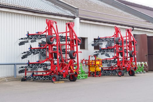 Vilnius, Lithuania - June 5, 2023: A red agricultural implement with numerous tines stands parked outside a building on a paved lot, its large wheels resting on the ground. The machinery is designed for farming and agricultural applications.