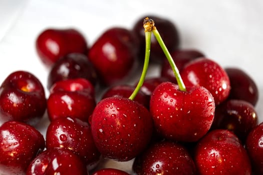 A handful of ripe cherries are arranged neatly on a clean, white tabletop surface, showcasing their vibrant color and freshness